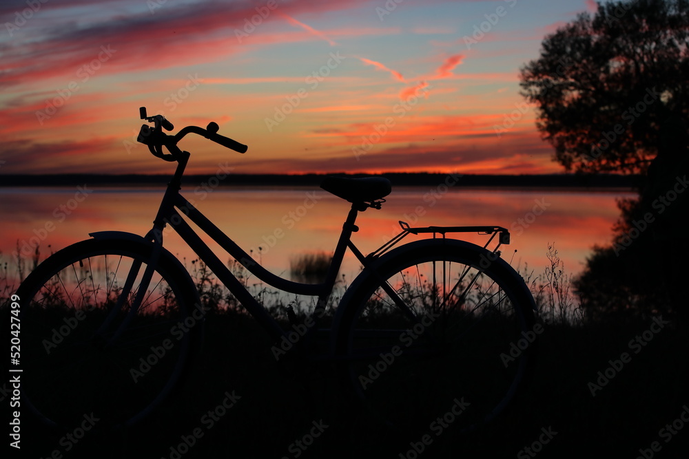 Obraz premium Sunset on the lake with a silhouette of a bicycle on the shore