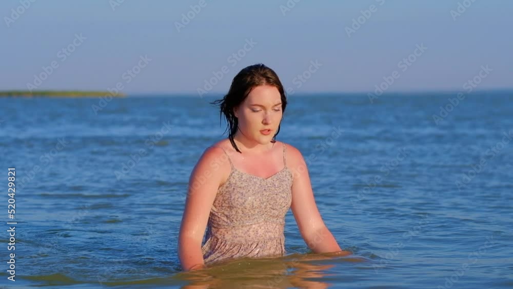 A young beautiful girl in a wet sundress comes out of the sea. A young beautiful girl in a wet sundress comes out of the sea.