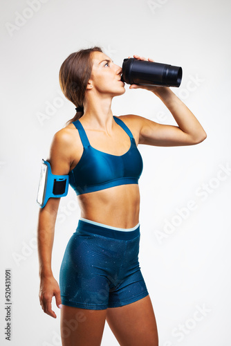 Portrait of a girl in sports outfit drinking water from a bottle. Female runner against gray background