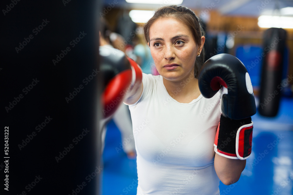 Hispanic boxer woman in boxing gloves is practicing different punches at gym