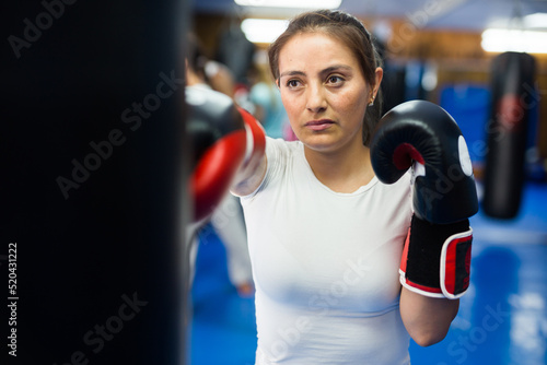 Hispanic boxer woman in boxing gloves is practicing different punches at gym © JackF