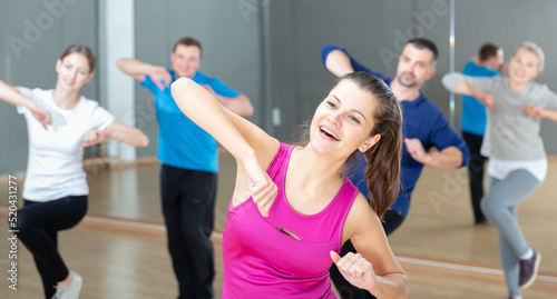 Portrait of young emotional woman doing exercises during group class in dance center