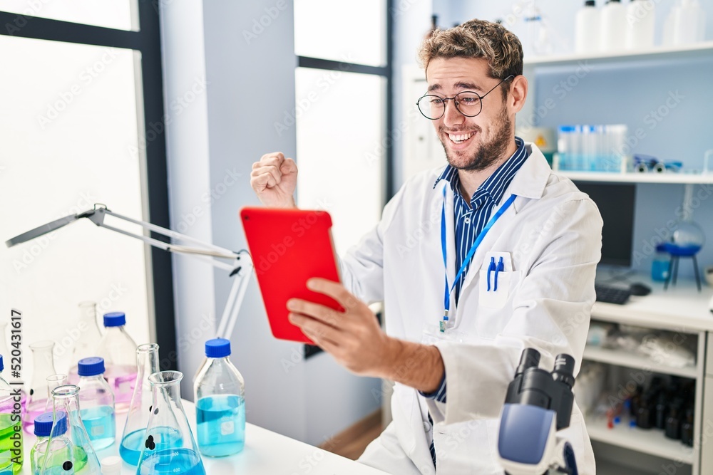 Hispanic man with beard working at scientist laboratory doing video call screaming proud, celebrating victory and success very excited with raised arm Hispanic man with beard working at scientist laboratory doing video call screaming proud, celebrating victory and success very excited with raised arm