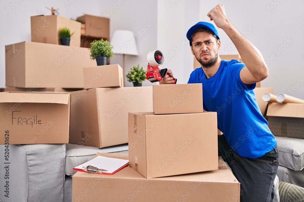 Fototapeta premium Hispanic man with beard working moving boxes annoyed and frustrated shouting with anger, yelling crazy with anger and hand raised