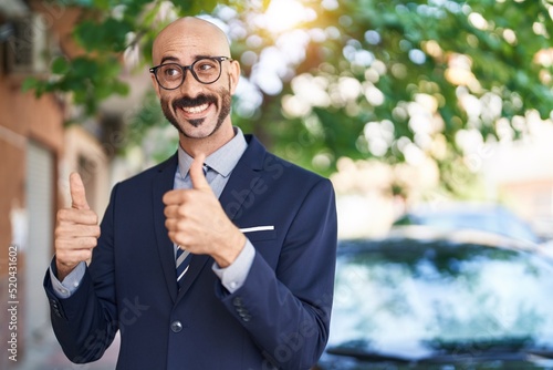 Young hispanic man executive smiling confident doing ok sign with thumbs up at street