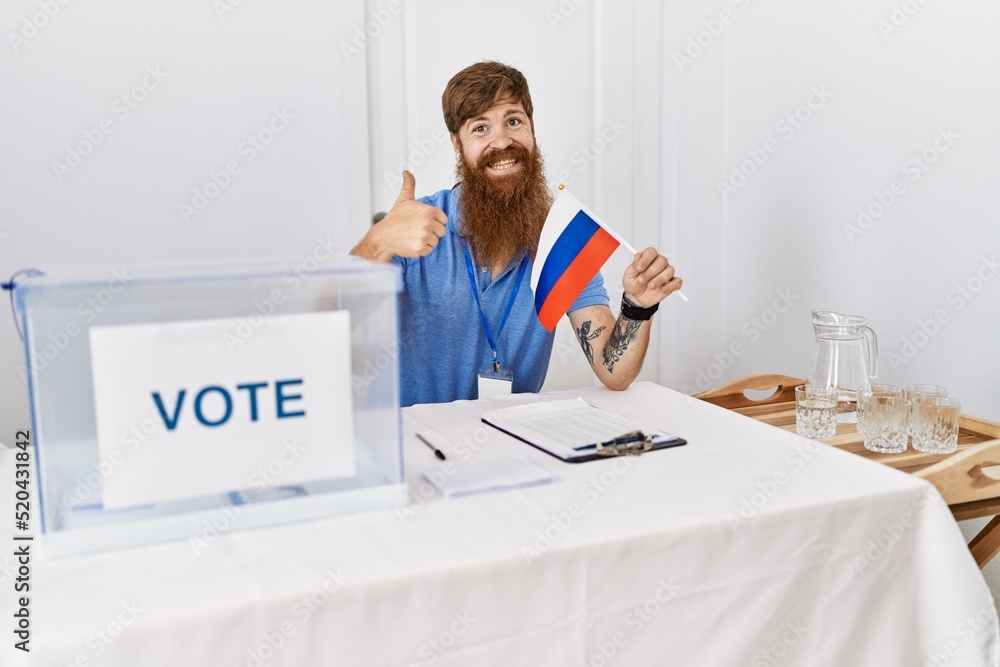Caucasian man with long beard at political campaign election holding russia flag smiling happy and positive, thumb up doing excellent and approval sign Caucasian man with long beard at political campaign election holding russia flag smiling happy and positive, thumb up doing excellent and approval sign
