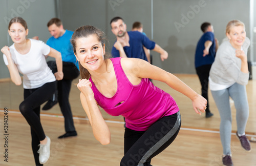 Smiling young female coach doing dance workout with adult group in fitness center