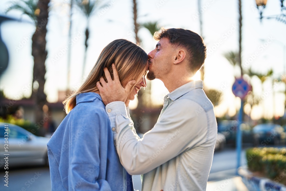 Young man and woman couple hugging each other and kissing standing at street