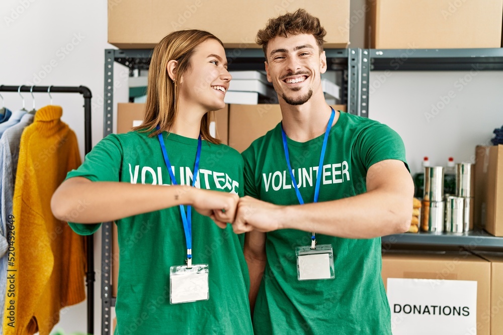 Obraz premium Young hispanic volunteer couple smiling happy bump fists at charity center.