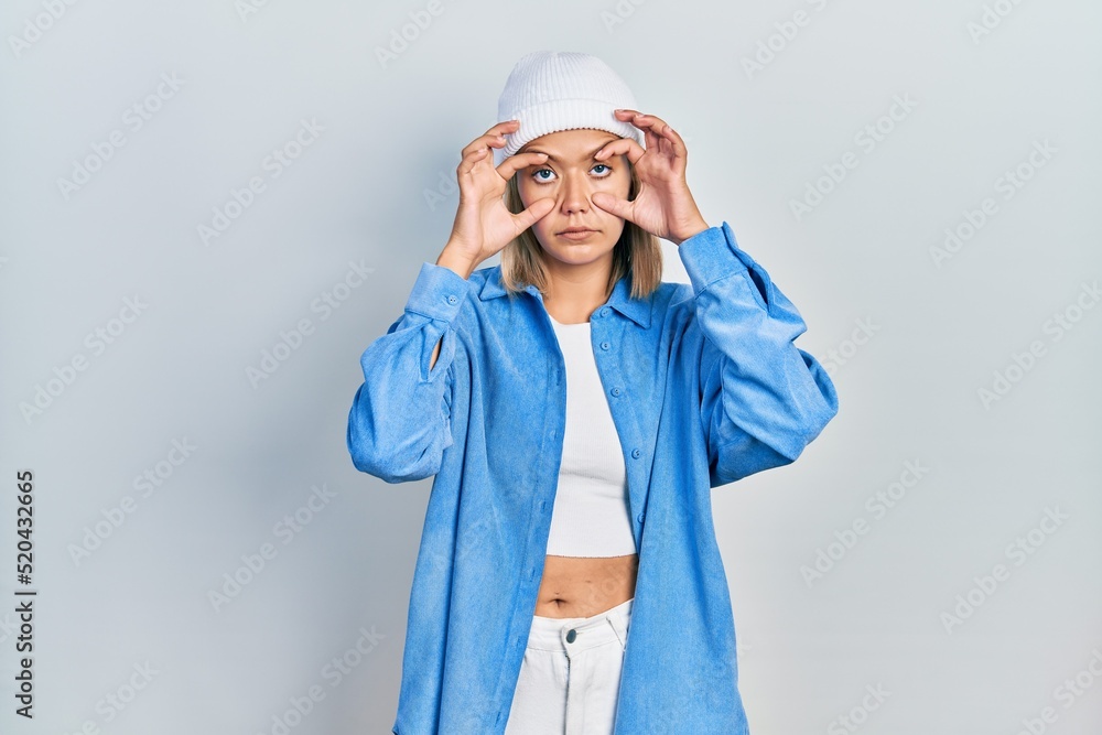 Beautiful blonde woman wearing wool hat trying to open eyes with fingers, sleepy and tired for morning fatigue Beautiful blonde woman wearing wool hat trying to open eyes with fingers, sleepy and tired for morning fatigue