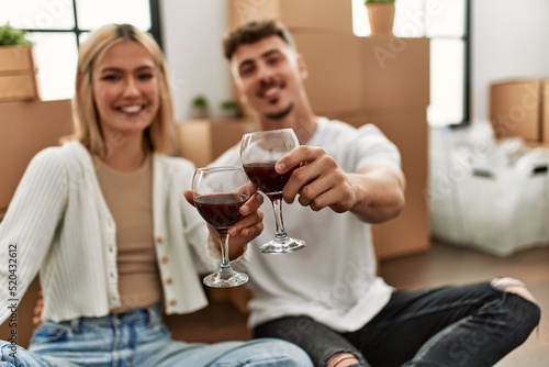 Young caucasian couple toasting with red wine glass sitting at new home. © Krakenimages.com