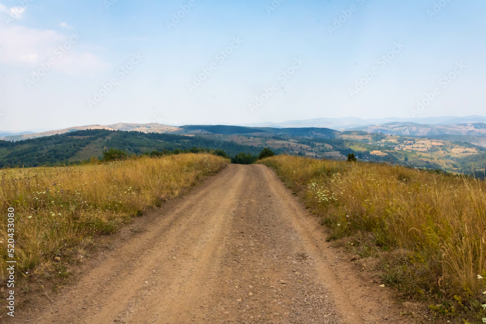 Dry grass field with dirt road and mountains in the distance, Zlatar mountain in Serbia