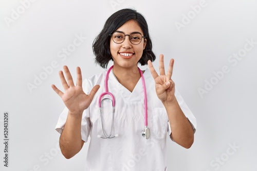 Young hispanic doctor woman wearing stethoscope over isolated background showing and pointing up with fingers number eight while smiling confident and happy.