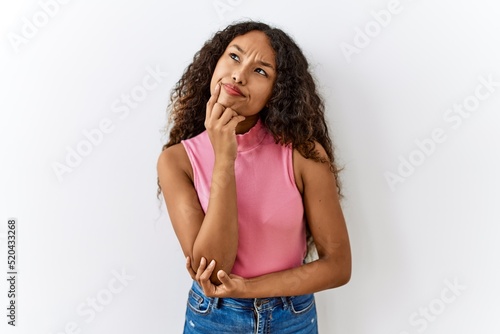 Beautiful hispanic woman standing over isolated background with hand on chin thinking about question, pensive expression. smiling with thoughtful face. doubt concept.