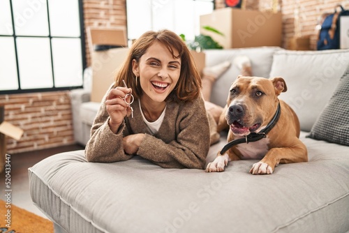 Young caucasian woman holding key of new house lying on sofa with dog at new home