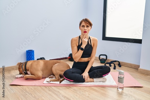 Young beautiful woman sitting on yoga mat thinking concentrated about doubt with finger on chin and looking up wondering