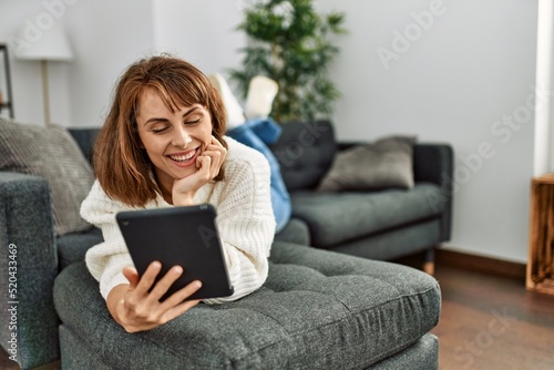 Young caucasian woman using touchpad lying on sofa at home
