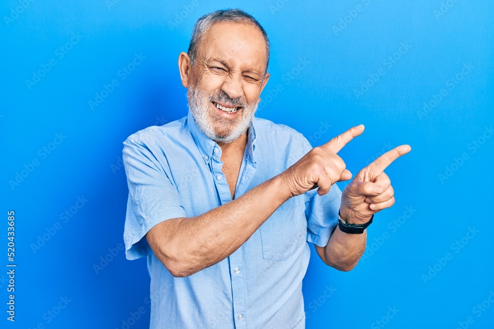 Handsome senior man with beard wearing casual blue shirt smiling and looking at the camera pointing with two hands and fingers to the side. Handsome senior man with beard wearing casual blue shirt smiling and looking at the camera pointing with two hands and fingers to the side.