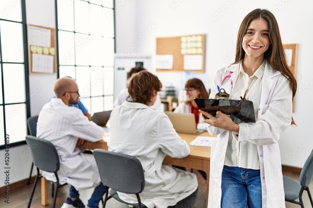 Fototapeta premium Group of young doctor working at the clinic office. Woman smiling happy writing on clipboard.