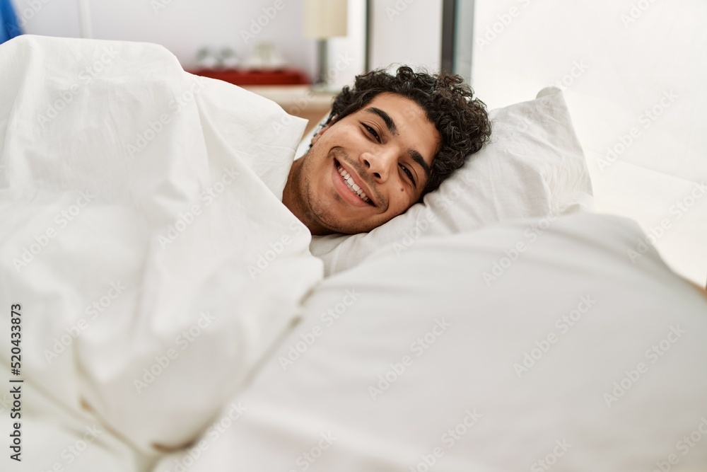 Young hispanic man smiling happy lying on the bed at bedroom.