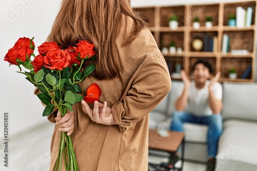 Woman suprising man with bouquet of roses at home. photo