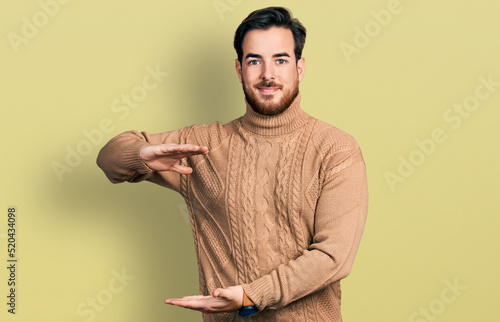 Young hispanic man wearing casual clothes gesturing with hands showing big and large size sign, measure symbol. smiling looking at the camera. measuring concept.