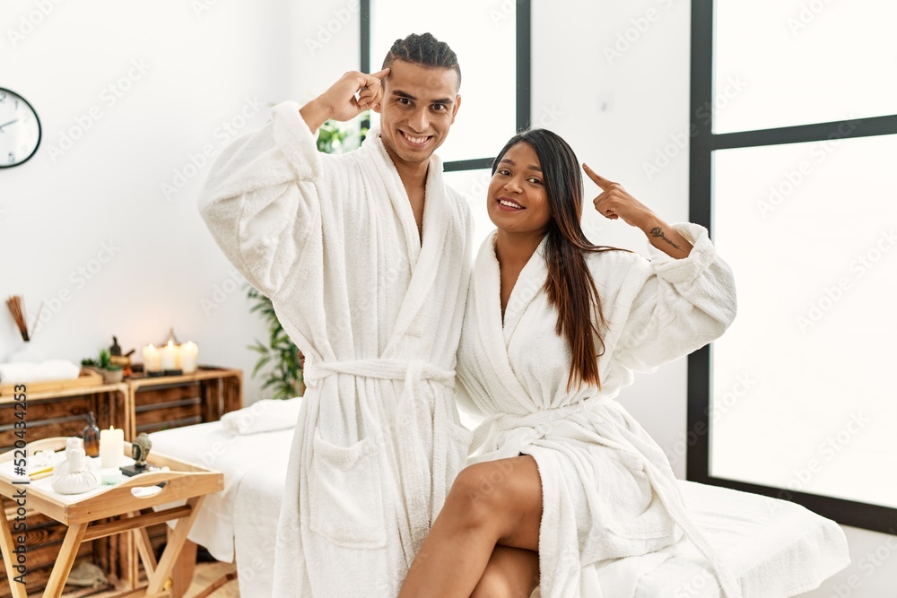 Young latin couple wearing towel standing at beauty center smiling pointing to head with one finger, great idea or thought, good memory Young latin couple wearing towel standing at beauty center smiling pointing to head with one finger, great idea or thought, good memory