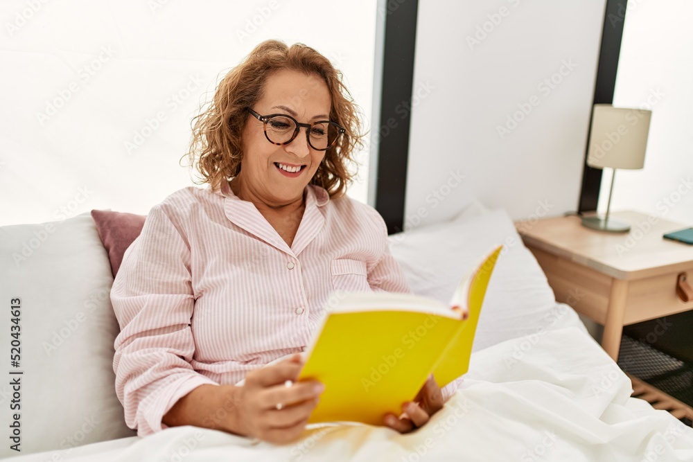Middle age caucasian woman reading book sitting on the bed at bedroom. Middle age caucasian woman reading book sitting on the bed at bedroom.