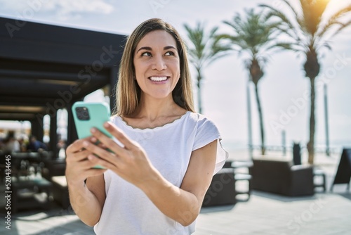 Wallpaper Mural Young hispanic woman smiling confident using smartphone at street Torontodigital.ca