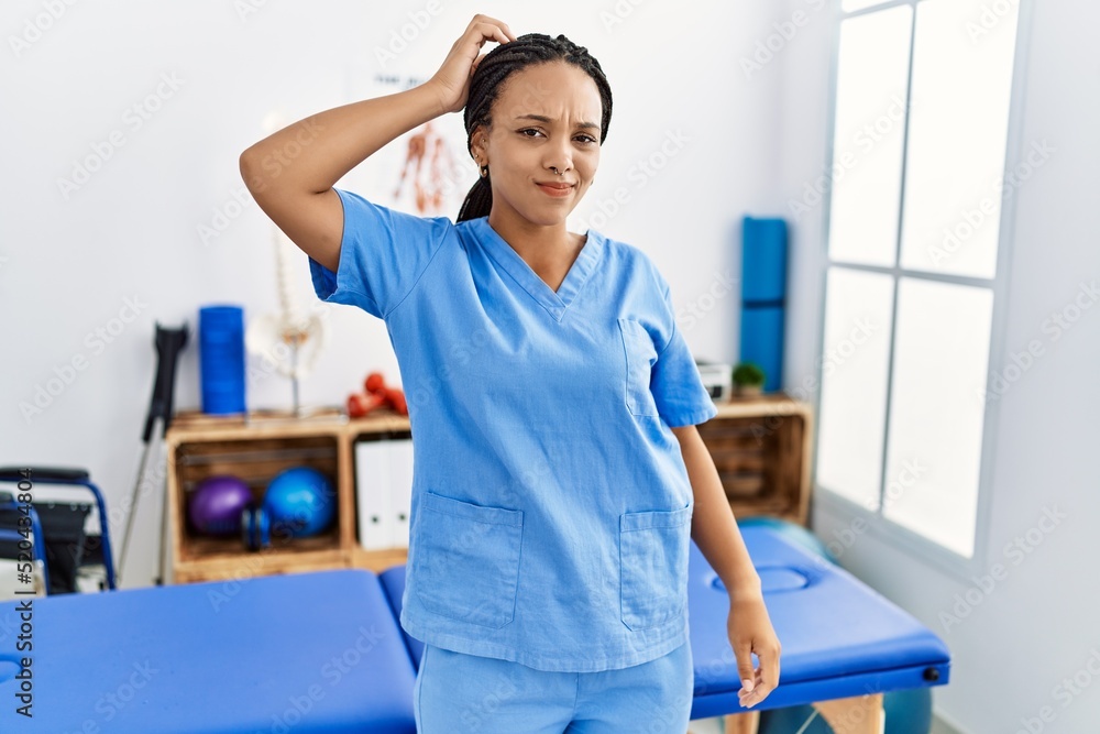 Young african american woman working at pain recovery clinic confuse and wonder about question. uncertain with doubt, thinking with hand on head. pensive concept. Young african american woman working at pain recovery clinic confuse and wonder about question. uncertain with doubt, thinking with hand on head. pensive concept.