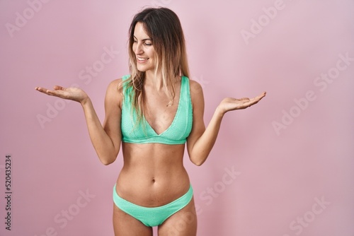 Young hispanic woman wearing bikini over pink background smiling showing both hands open palms, presenting and advertising comparison and balance © Krakenimages.com