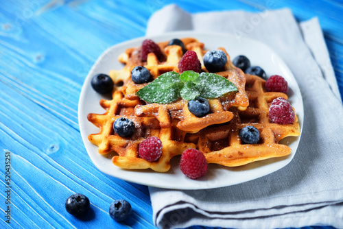 Waffles with blueberries and raspberries for breakfast over blue wooden table.