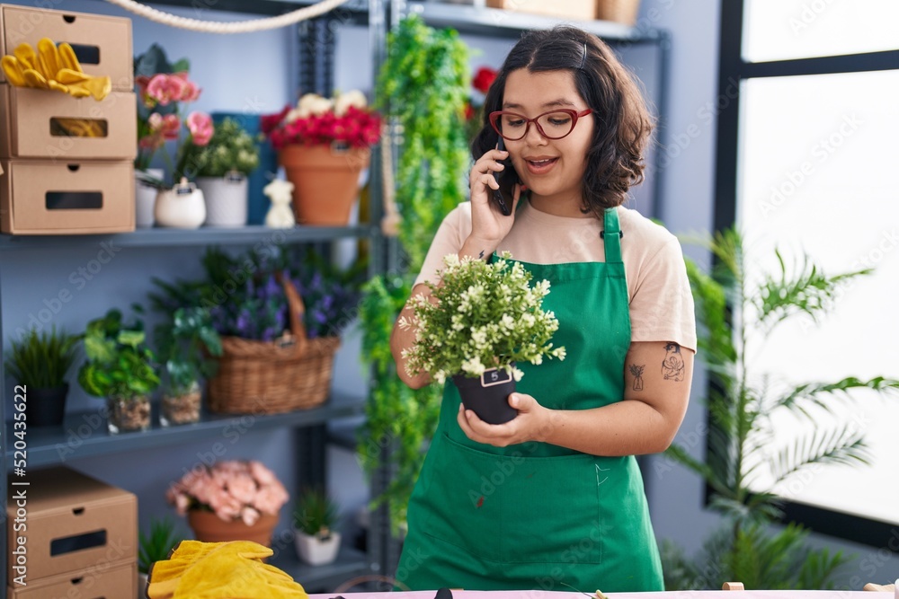 Young woman florist talking on smartphone holding plant pot at florist