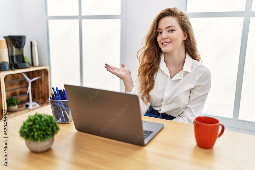 Young caucasian woman working at the office using computer laptop smiling cheerful presenting and pointing with palm of hand looking at the camera. Young caucasian woman working at the office using computer laptop smiling cheerful presenting and pointing with palm of hand looking at the camera.