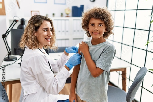 Valokuva Mother and son wearing doctor uniform putting band aid on child arm at clinic