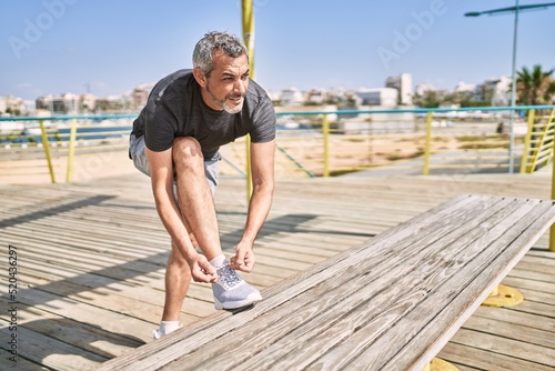 Fotografija Middle age hispanic man smiling confident tying shoe at street