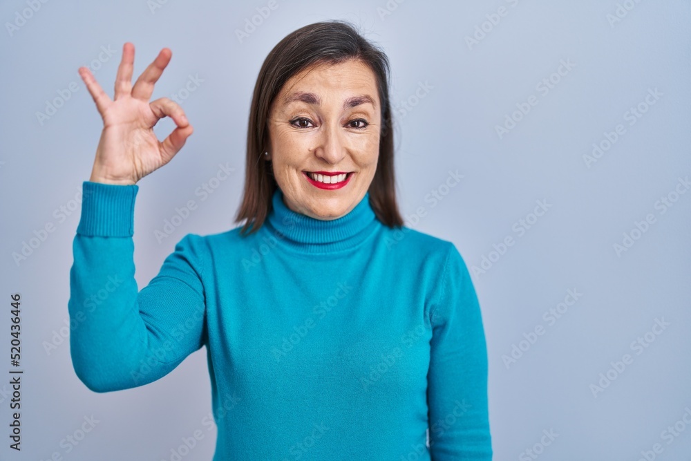Middle age hispanic woman standing over isolated background smiling positive doing ok sign with hand and fingers. successful expression. Middle age hispanic woman standing over isolated background smiling positive doing ok sign with hand and fingers. successful expression.