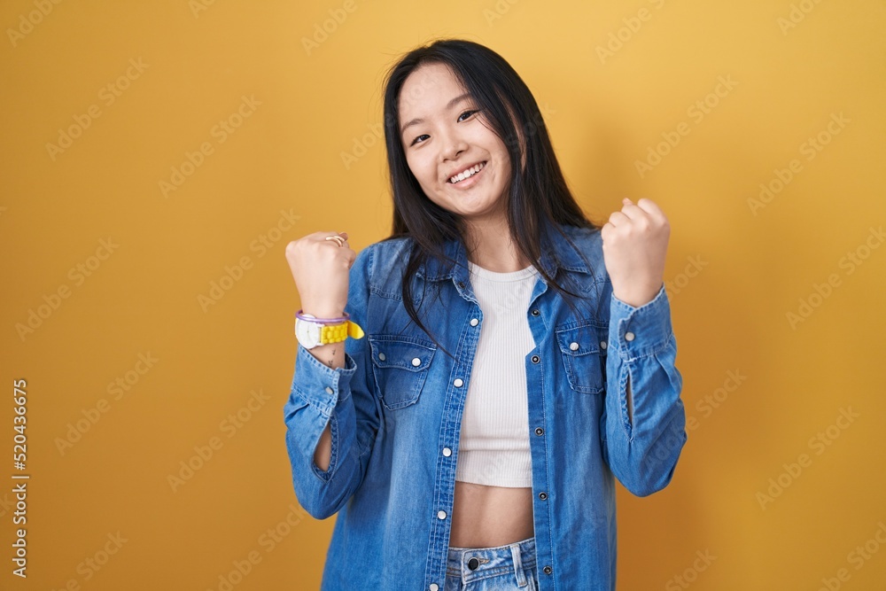 Young asian woman standing over yellow background celebrating surprised and amazed for success with arms raised and eyes closed. winner concept. Young asian woman standing over yellow background celebrating surprised and amazed for success with arms raised and eyes closed. winner concept.