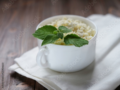 Cottage cheese with mint in a white bowl over wooden baclground.