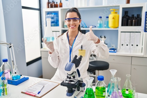 Hispanic woman working at scientist laboratory smiling happy and positive  thumb up doing excellent and approval sign