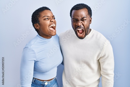 Young african american couple standing over blue background angry and mad screaming frustrated and furious  shouting with anger. rage and aggressive concept.
