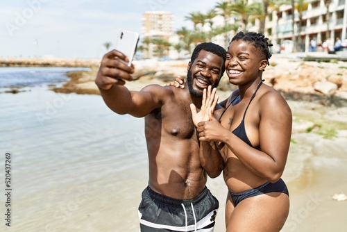 Young african american tourist couple wearing swimwear making selfie by the smartphone at the beach.