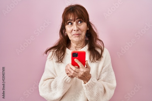 Middle age hispanic woman using smartphone typing message smiling looking to the side and staring away thinking.