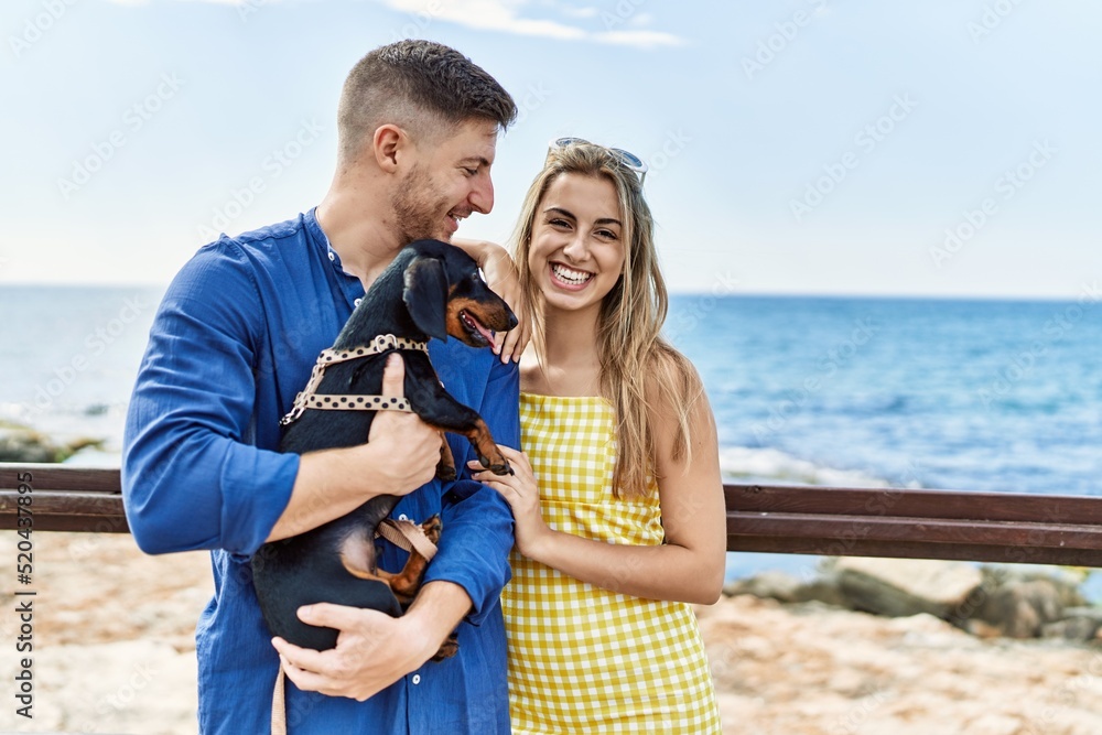Young caucasian couple smiling happy and hugging with dog at the beach.