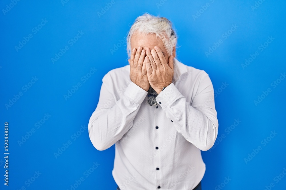 Middle age man with grey hair standing over blue background with sad expression covering face with hands while crying. depression concept. Middle age man with grey hair standing over blue background with sad expression covering face with hands while crying. depression concept.