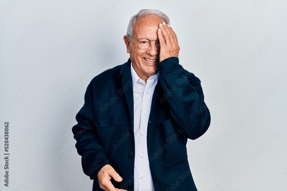 Senior man with grey hair wearing casual style and glasses covering one eye with hand, confident smile on face and surprise emotion. Senior man with grey hair wearing casual style and glasses covering one eye with hand, confident smile on face and surprise emotion.
