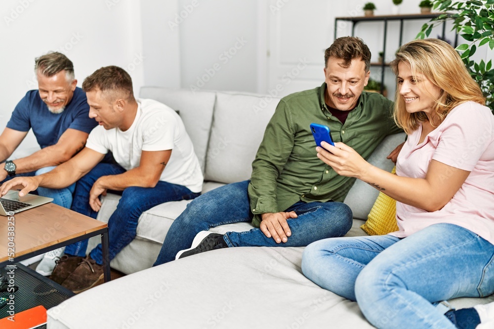 Group of middle age friends smiling happy using smartphone and laptop sitting on the sofa at home.