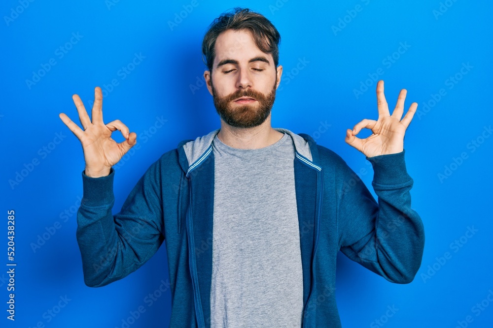 Naklejka premium Caucasian man with beard wearing casual sweatshirt relax and smiling with eyes closed doing meditation gesture with fingers. yoga concept.
