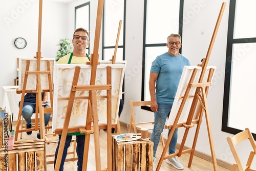 Group of middle age people artist at art studio looking positive and happy standing and smiling with a confident smile showing teeth