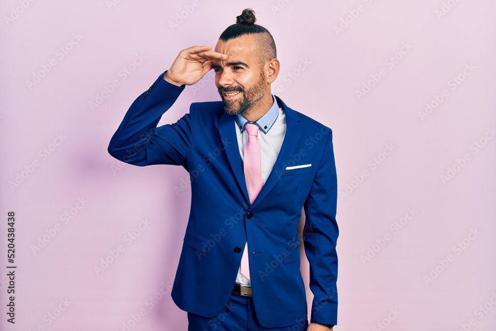 Young hispanic man wearing business suit and tie very happy and smiling looking far away with hand over head. searching concept. Young hispanic man wearing business suit and tie very happy and smiling looking far away with hand over head. searching concept.